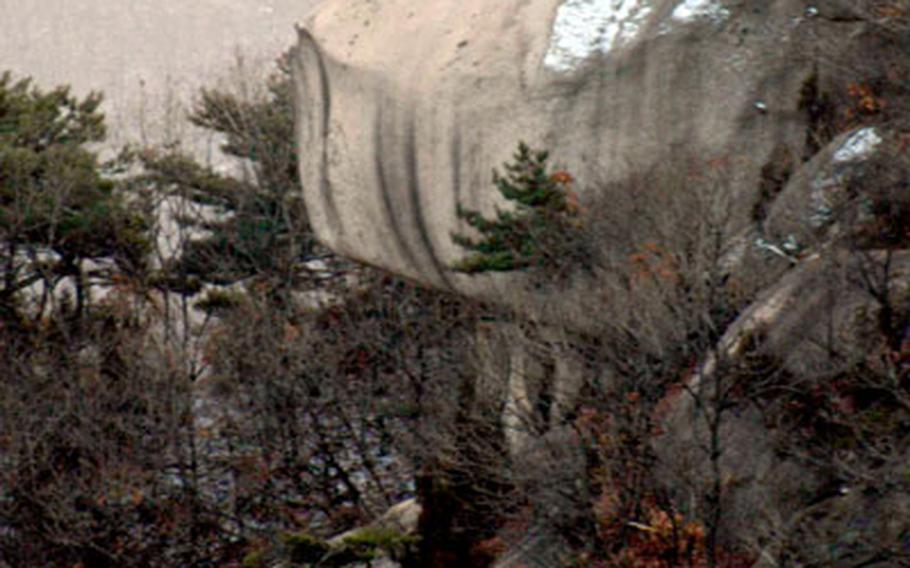 Hikers stand on a massive boulder in the park.