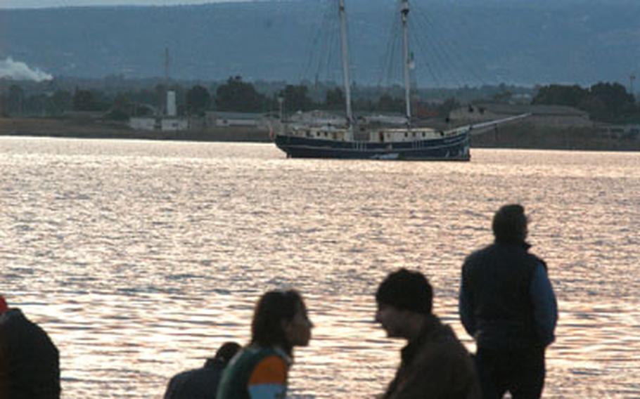 Young lovers and fishermen take in the sunset over the Sicilian coast along Syracuse&#39;s Porta Grande, or grand port, as a twin-masted sailboat sits at anchor in the harbor.