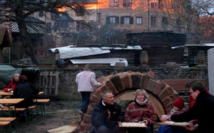 The colors of a fire echo the sunset colors on the walls of Büdingen&#39;s castle as visitors of the Christmas market eat  in the courtyard of the castle.