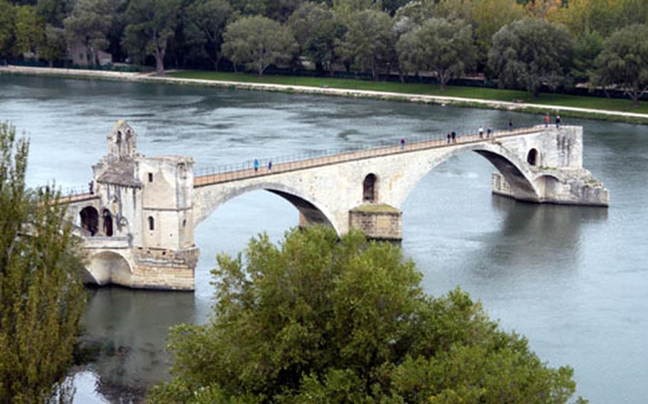 The St. Bénezet Bridge in Avignon, made famous by the song "Sur le Pont d&#39;Pvignon....", as seen from the Rocher des Doms garden. The bridge dates back to the 12th century and was 2953 feet long with 22 arches, but now only a few arches reach out over the Rhone. The bank at top is not the other side, but an island in the middle of the river.