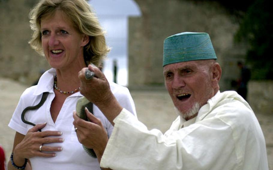 Jutta Huser, a tourist from Germany, calmly allows a Moroccan snake charmer’s cobra to circle around her neck as the charmer entertains a crowd in Tangier.