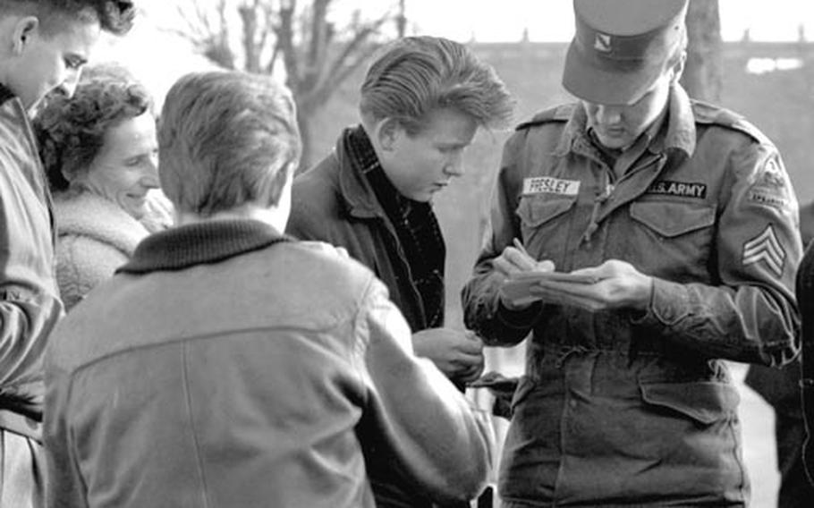 Sgt. Elvis Presley, of the 1st Battalion, 32nd Armor Regiment, 3rd Armored Division at Ray Barracks, signs autographs for Friedberg, Germany, residents as he arrives for an interview in February, 1960.