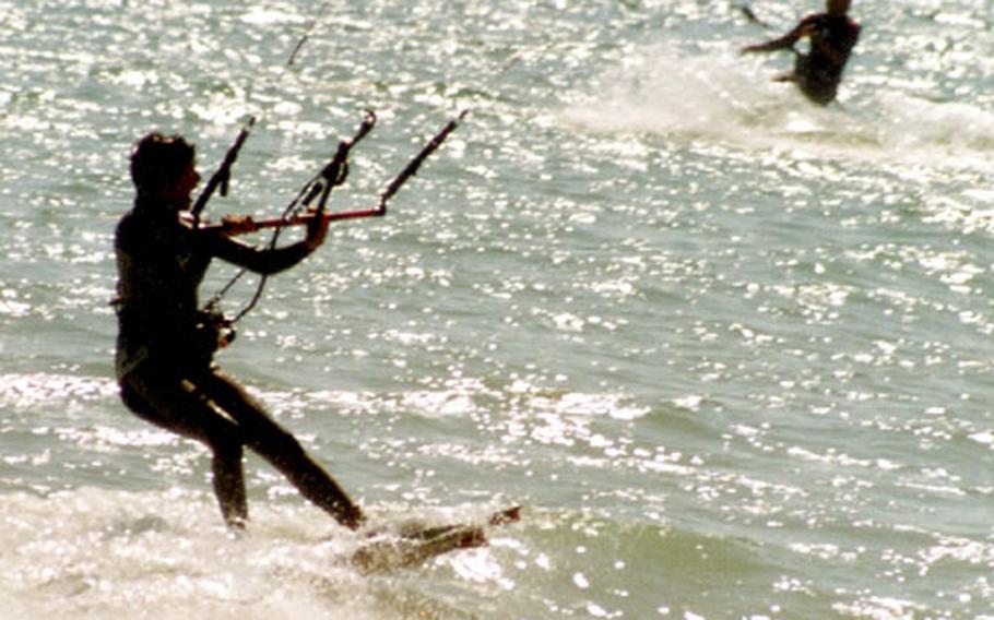 A kitesurfer hangs on tight to the harness and glides across sparkling waves at Sancti Petri.