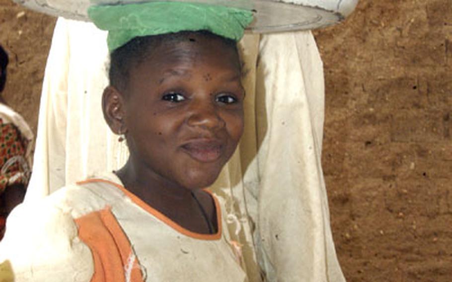 A local girl effortlessly carries spices and grains on her head through downtown Agadez.