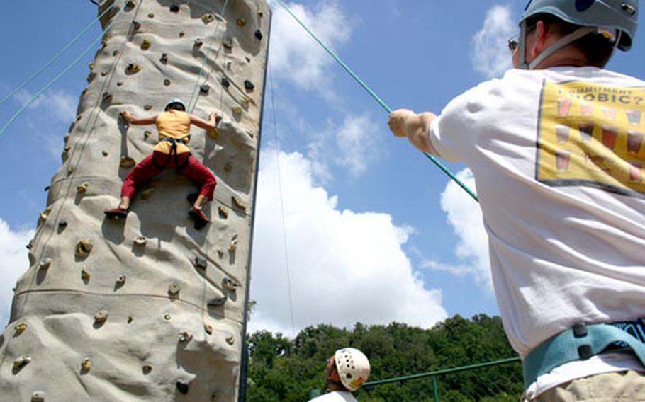 Stuart Misfeldt holds belay while his wife, Rachel Myaing-Misfeldt, climbs the rock wall at Carney Park in Naples, Italy. Below her, instructor Michael Dong offers advice on where she can place her feet and hands to help her shimmy up the wall.