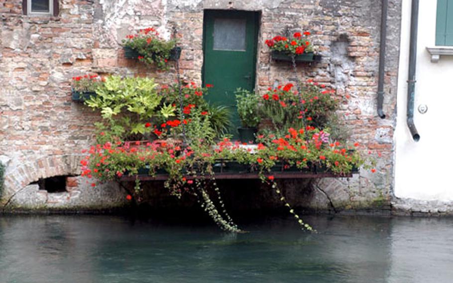 A small flower-filled terrace jutting out over a canal in Treviso, Italy.