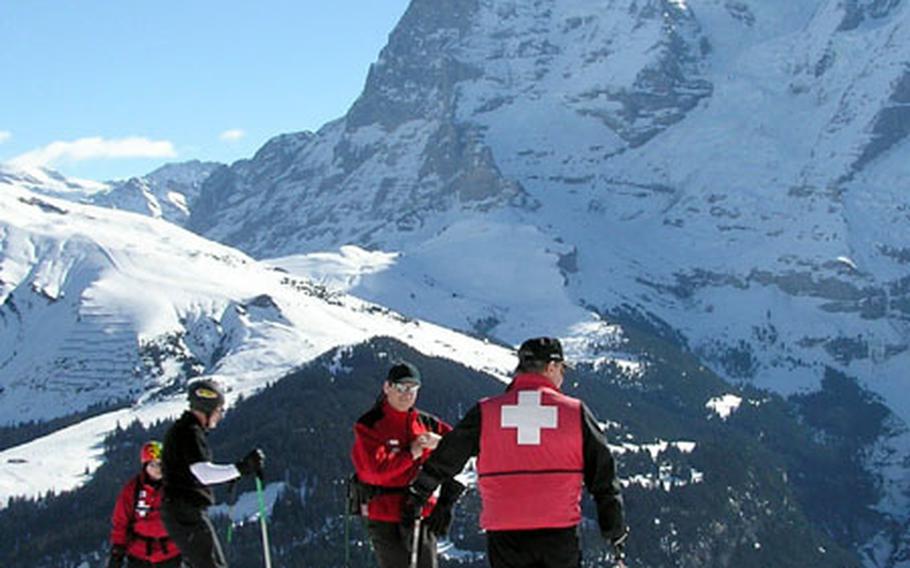 Ski Patrol instructors Tom McCoy and Mike Staszewski, back to camera, take a break in the mountains of Winteregg in Switzerland&#39;s Lauterbrunnen Valley during candidate training in March. The Eiger massif and Kleine Scheidegg are in the background.