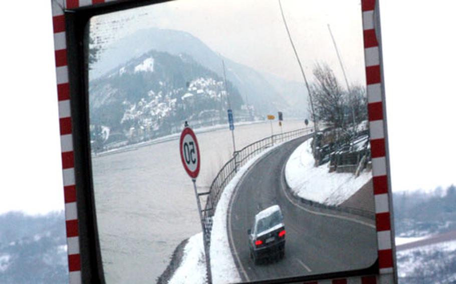 A single car, reflected in a traffic mirror, travels through the quiet Rhine River valley.