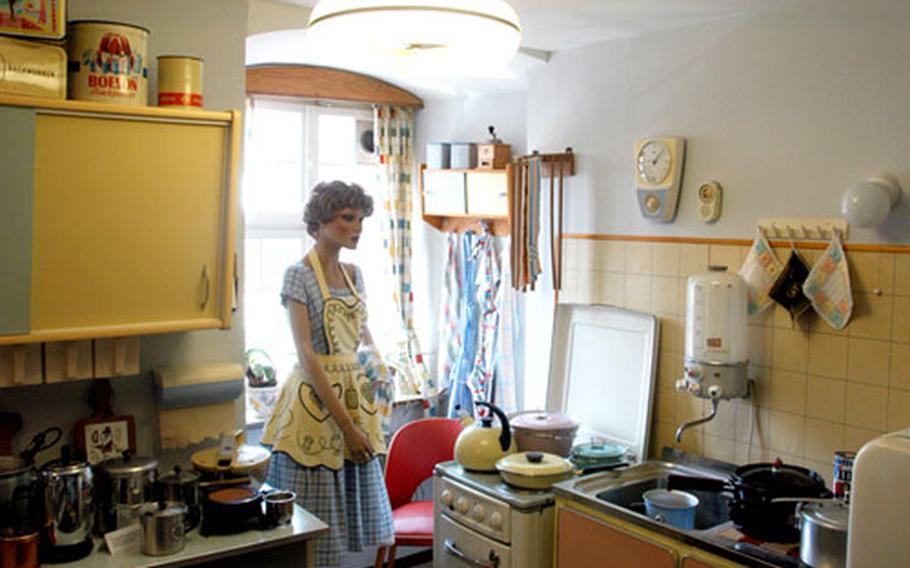 A mannequin dressed as a typical German housewife stands in her pastel-colored kitchen.