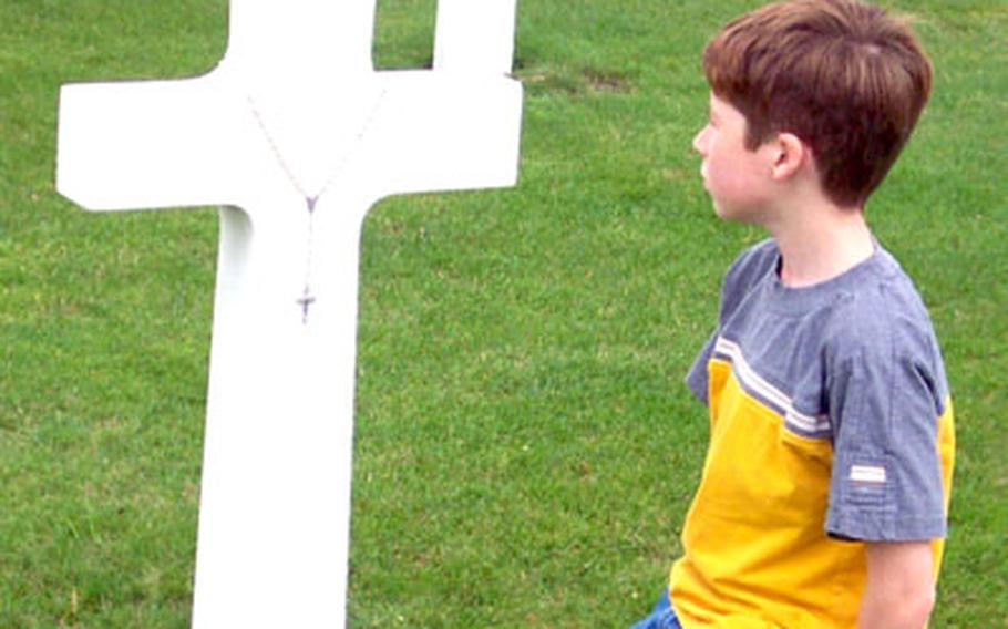 Wesley Barnes, 10, spots a cross draped with a rosary, possibly left as a reminder of prayers said on behalf of the veteran buried there.