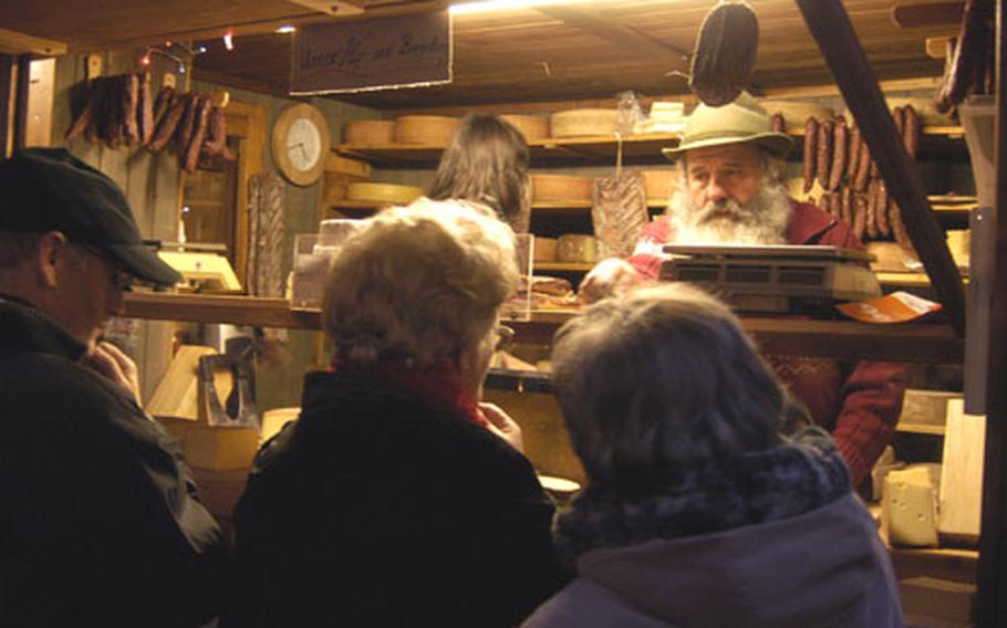 a vendor selling Swiss mountain cheeses and sausages offers a sample to a visitor to the Basel Christmas market.
