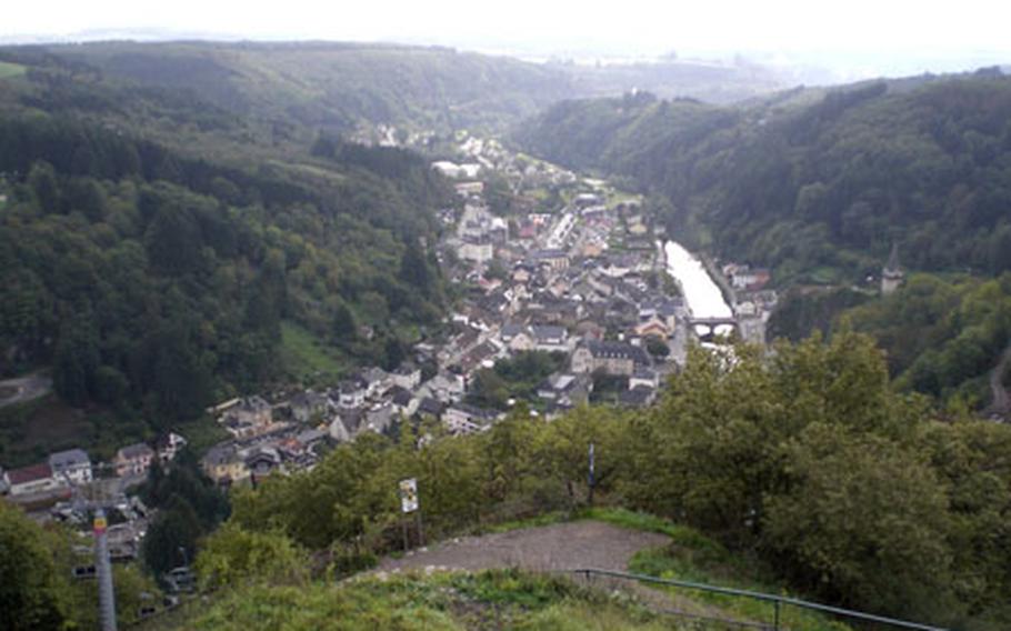 The chairlift -- one of its towers is shown at left -- whisks passengers across the River Our before beginning its ascent. From the summit the castle, seen through the trees at right, and the town of Vianden with the river running through it, are both visible.