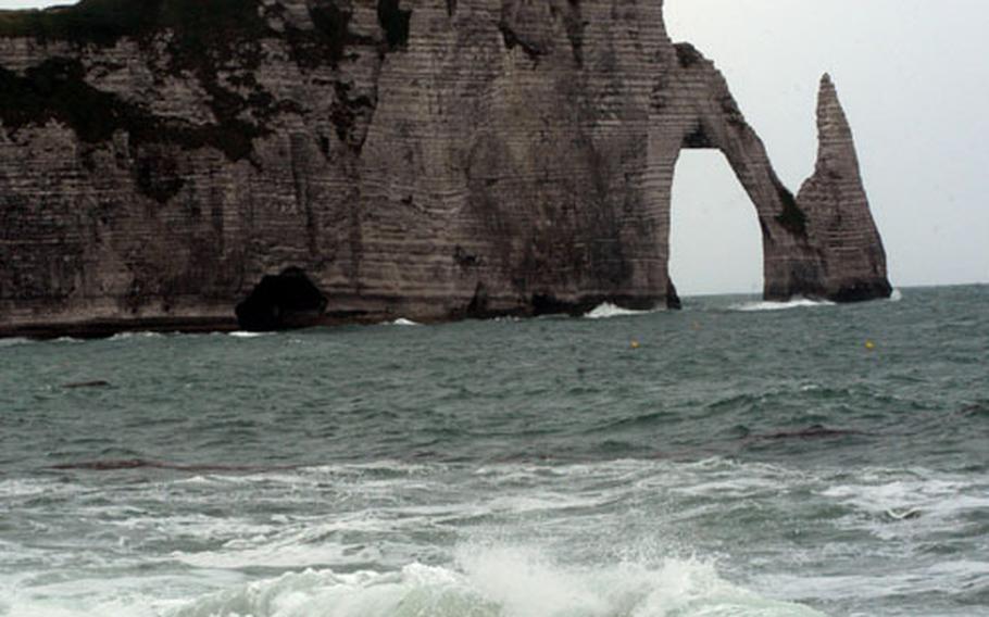 Visitors atop the Falaise d&#39; Aval rock formation on the Côte d Albâtre are barely visible as they walk to the end of the formation for a closer look at the rock needle Aiguille d’Étretat rising from the surf.