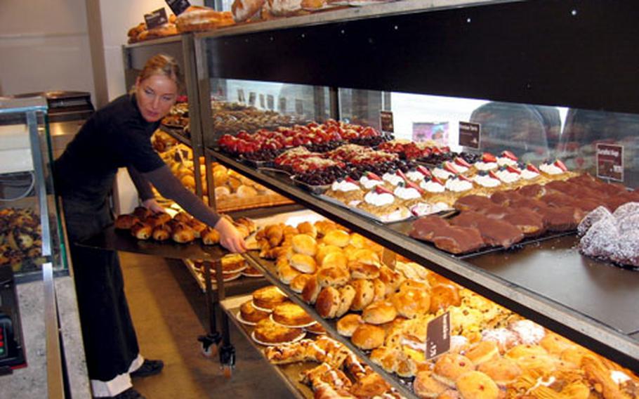 A "bakery maiden" replenishes the supply of pastry in a storefront window.