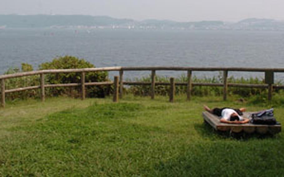 A Japanese man stretches out on a bench during a hot summer day on Monkey Island.