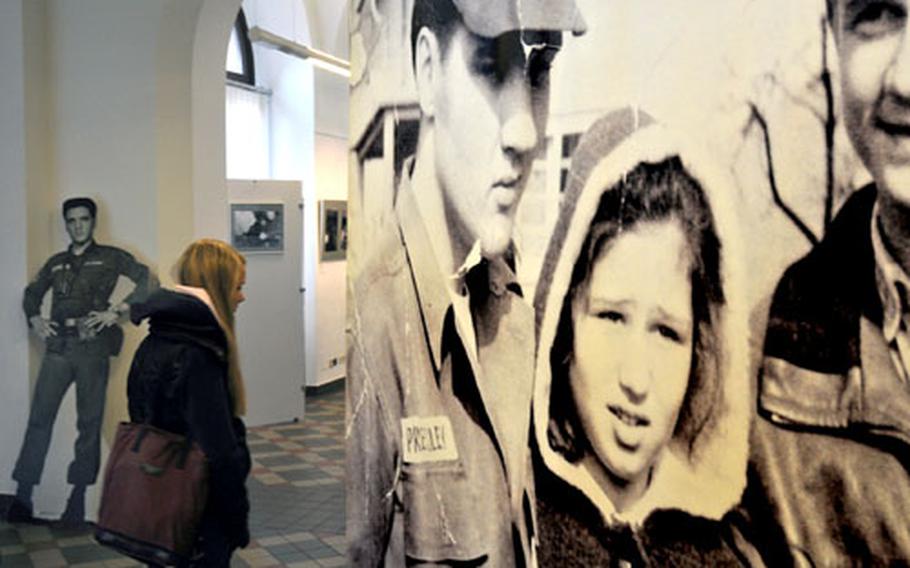 A current fan of Elvis Presley walks past a large poster of the King posing with some 1950s fans.