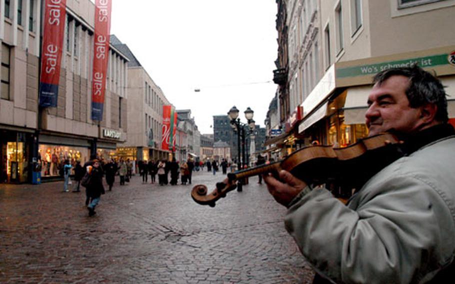 A violinist plays for the crowd on Trier&#39;s pedestrian shopping area. In the distance is the Porta Nigra, a Roman city gate from the second century.
