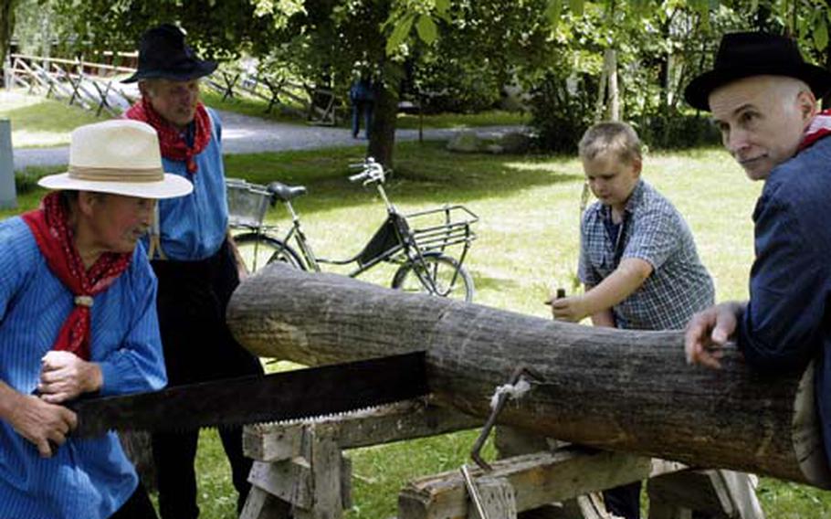 A museum worker shows a young visitor how much work was involved in cutting logs with a hand saw.
