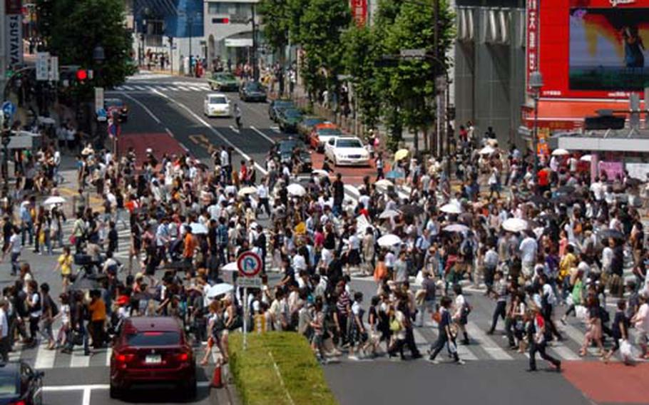 Pedestrians walk across the five-way scramble crossing in Shibuya. All the traffic lights turn red at the same time, and pedestrians cross the street simultaneously.