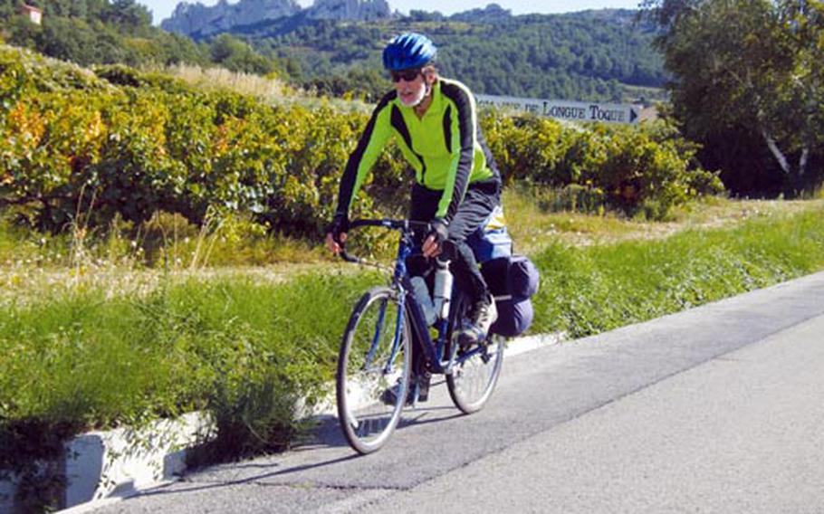The writer’s husband, Bicycle Bob, cycles through France’s Côtes du Rhône vineyards, with mountains in the background. As much as he enjoys pedaling up the local hills, he’s happy to leave the big ones to the professionals.