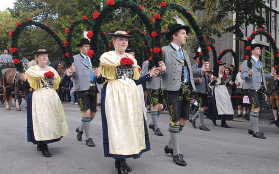 A folklore group in traditional Bavarian costumes marches beneath flowered arches in the parade.