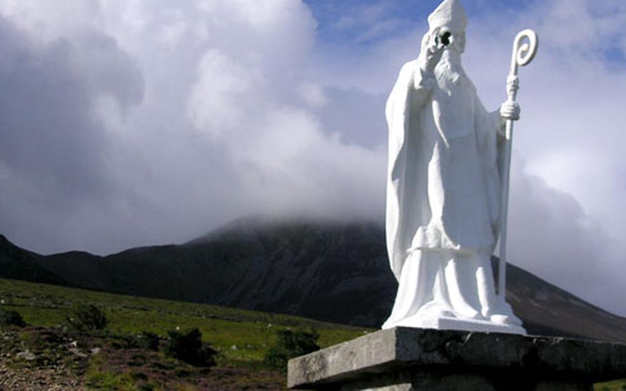 A statue of St. Patrick stands in front of Crough Patrick, Ireland's holy mountain. The top is hidden by clouds.