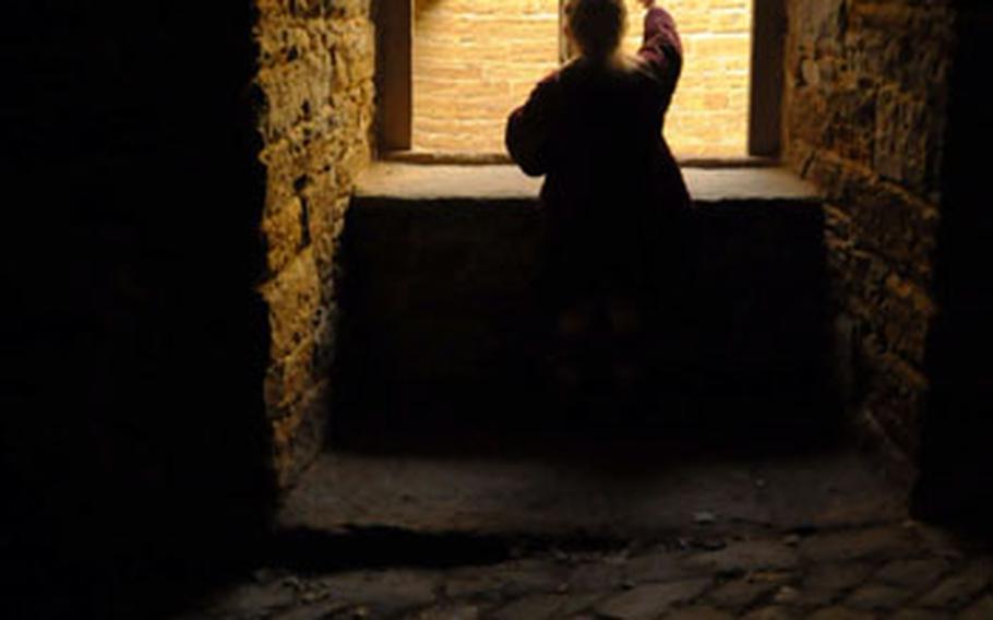 A young girl peers into an inner garden from a covered road on the Hohenzollern Castle grounds. The road leads to the main courtyard of the castle, where a gift shop, beer garden and chapel can be found.