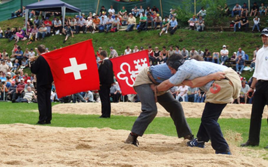 "Schwingen" wrestlers hang onto their opponent's shorts as they try to throw the other to the ground and then his shoulder while still hanging onto his shorts. Flag throwers, who entertain the spectators between bouts, await their turn to perform. 
