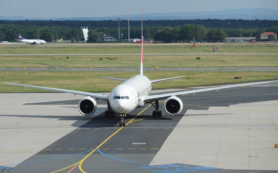 A Japan Airlines passenger jet rolls to its gate as a Lufthansa plane travels down the runway in the background. The three-fingered structure between the planes in the background is the Berlin Airlift Memorial.