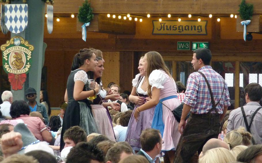 Wearing traditional Bavarian clothing, friends chat while standing on benches in one of Oktoberfest's giant beer tents.  