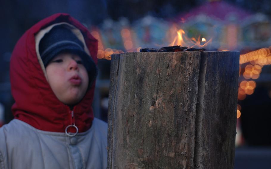 A child blows on a "Schwedenfackel" (Swedish torch), one of many used to warm the crowds at the market.