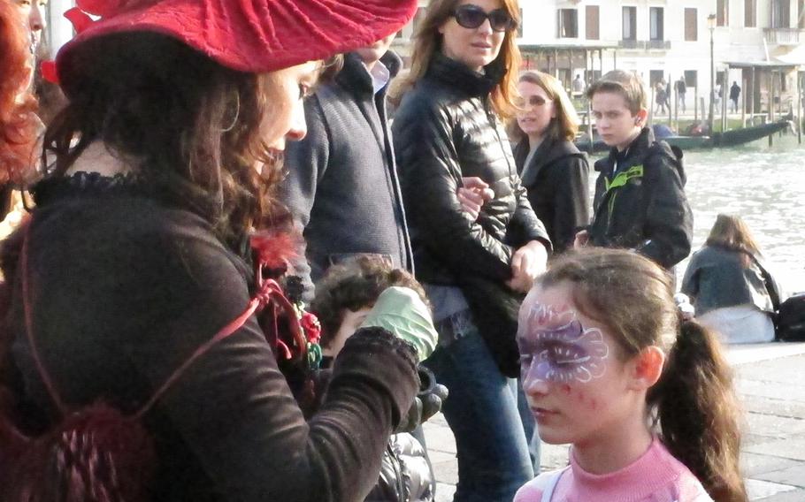 A costumed woman paints the face of a little girl at Carnevale in Venice on Sunday, Feb. 16, 2014.