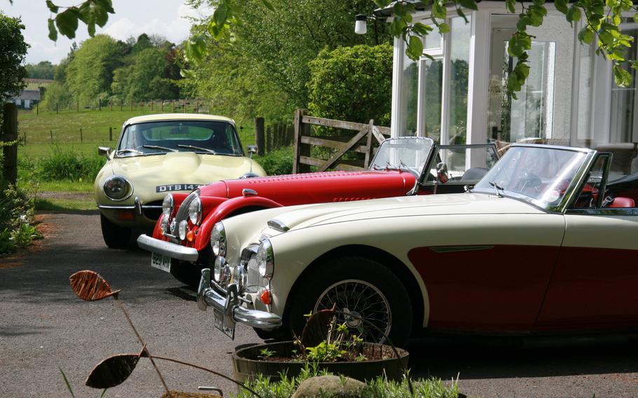 From back to front, an E-Type Jaguar, a Morgan and an Austin Healey dress up the countryside setting outside Caledonian Classic Car Hire, about a 50-minute drive from Edinburgh, Scotland.
