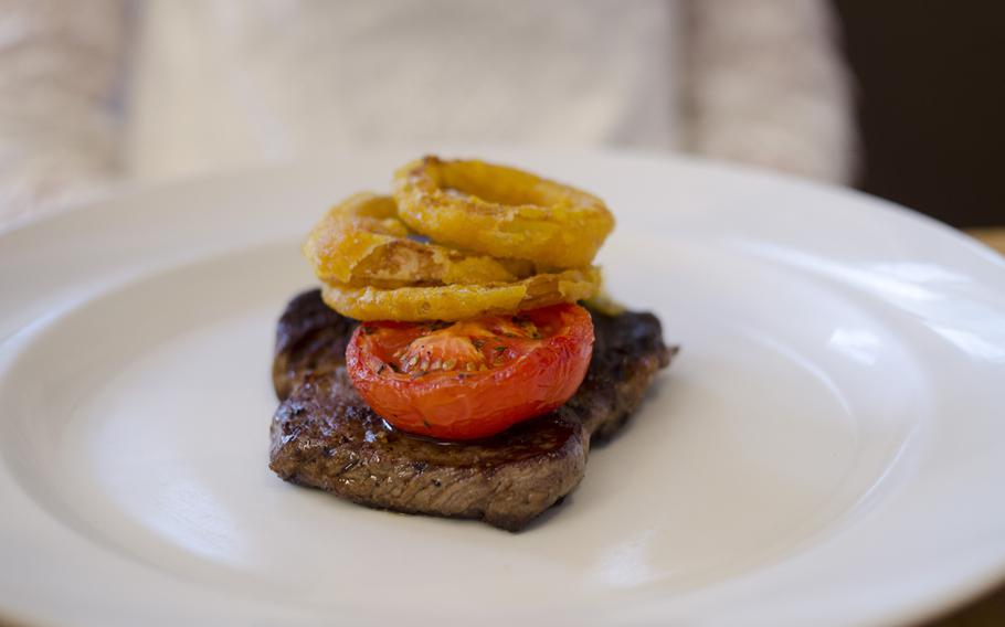 Steak is topped with onion rings, tomato and a mushroom at Rhubarb in Newmarket, England.