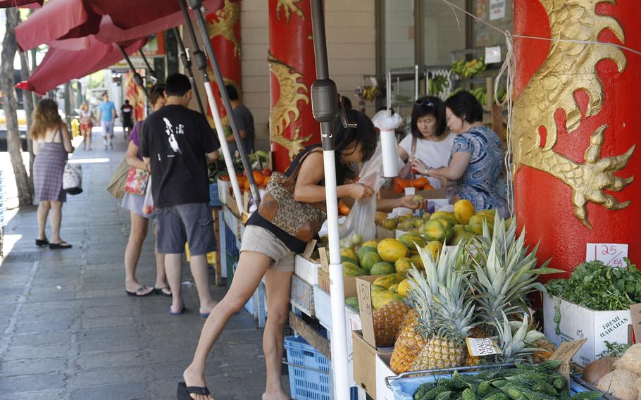 Shoppers pick through vegetables and fruit at a sidewalk vendor on a recent Sunday morning in Chinatown. Dozens of stores and stalls offer up fresh produce, some raised in the Hawiian islands.