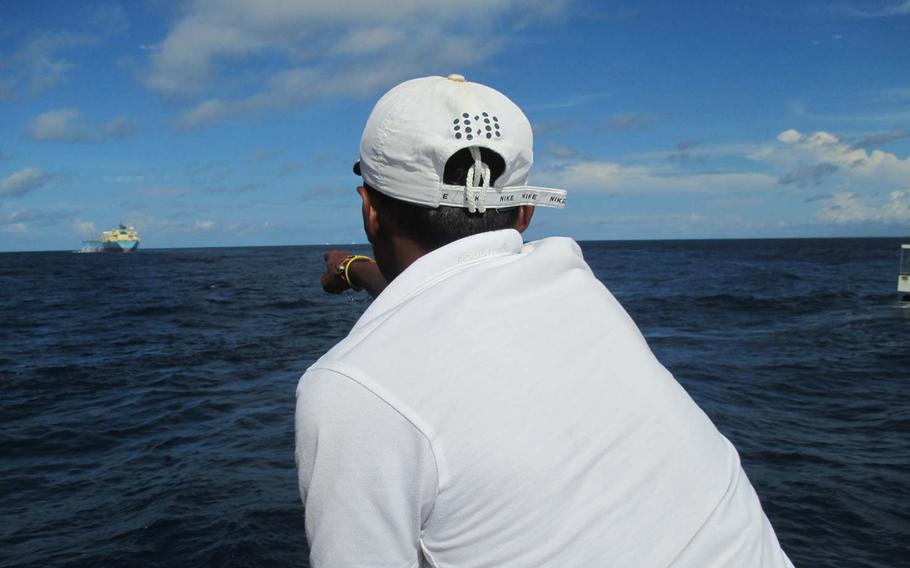  A crew member on the whale watching cruise points to a barely visible whale in the water.