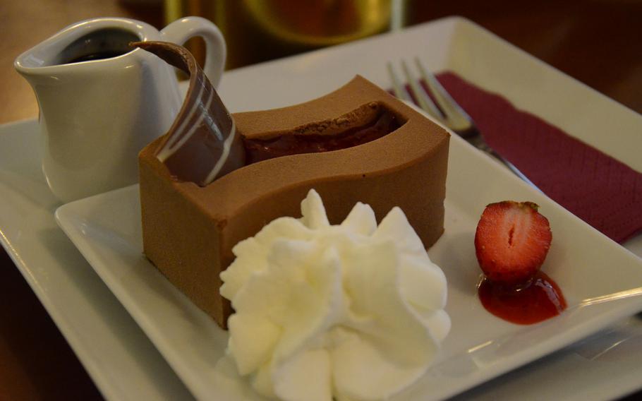 A chocolate mousse filled with strawberry jam is accompanied nicely by a cup of liquid chocolate, whip cream and half of a strawberry at Peratoner, a store in Pordenone, Italy known for its chocolate.