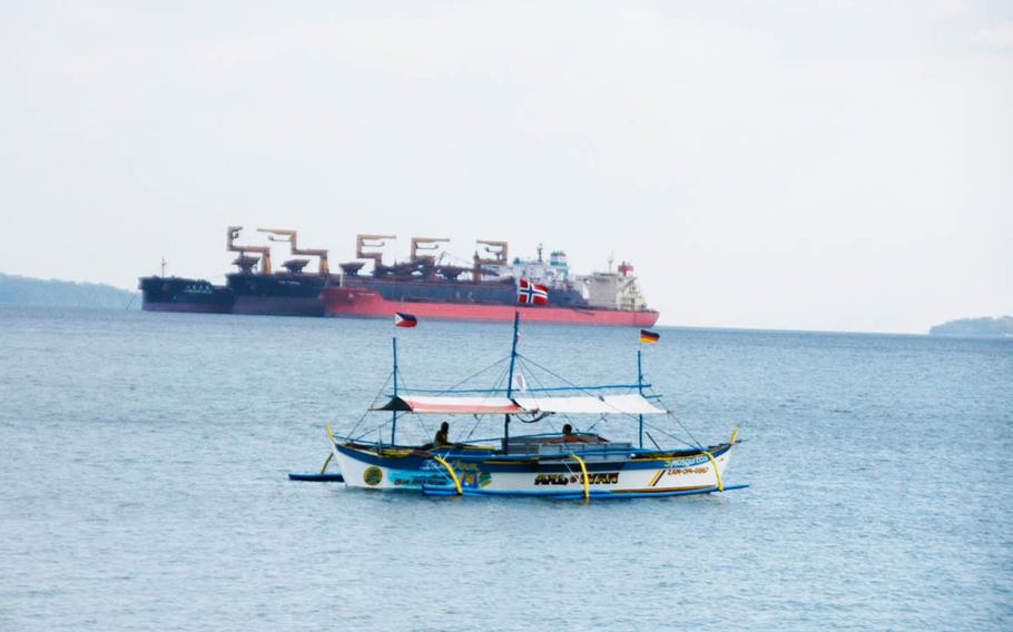 A tourist boat drifts in front of a massive commercial vessel near Baloy Beach in Subic Bay.