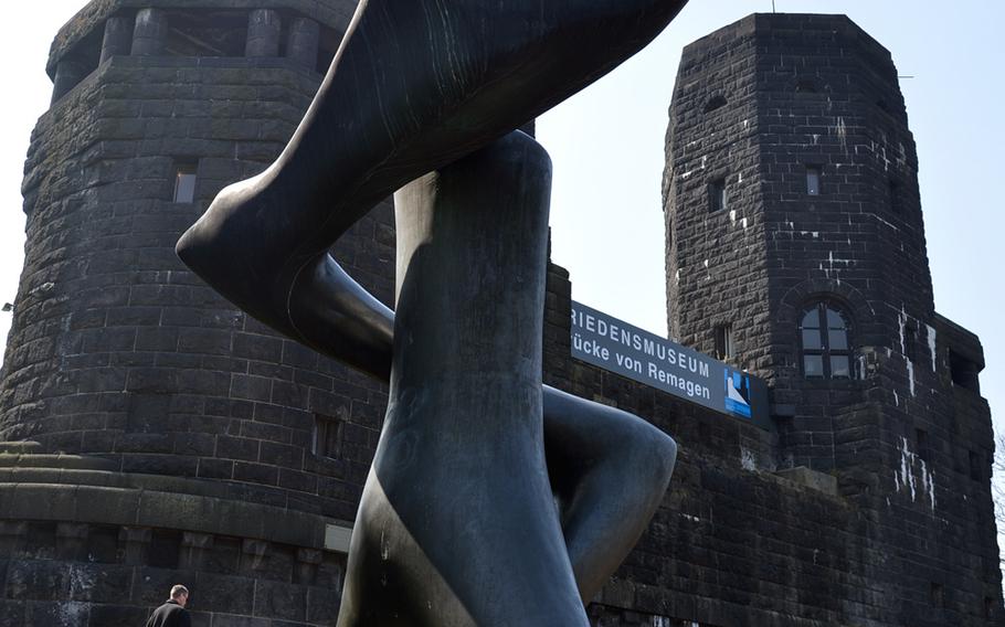 The sculpture "Liebeskraft" by Hungarian artist Lajos Barta stands on the west bank of the Rhine River in front of the remnants of the Ludendorff Bridge, which houses the Peace Museum. The bridge was captured by the U.S. Army on March 7, 1945, and used until it collapsed on March 17, 1945.