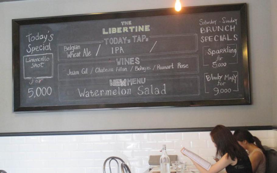 Customers peruse a menu while sitting underneath a blackboard announcing drink specials at Libertine Bar and Kitchen. The American-style menu offers upscale and at times creative takes on comfort food, from a gorgonzola- and hickory-smoked bacon-topped lamb burger to a salad with citrus and lavender-marinated beets.