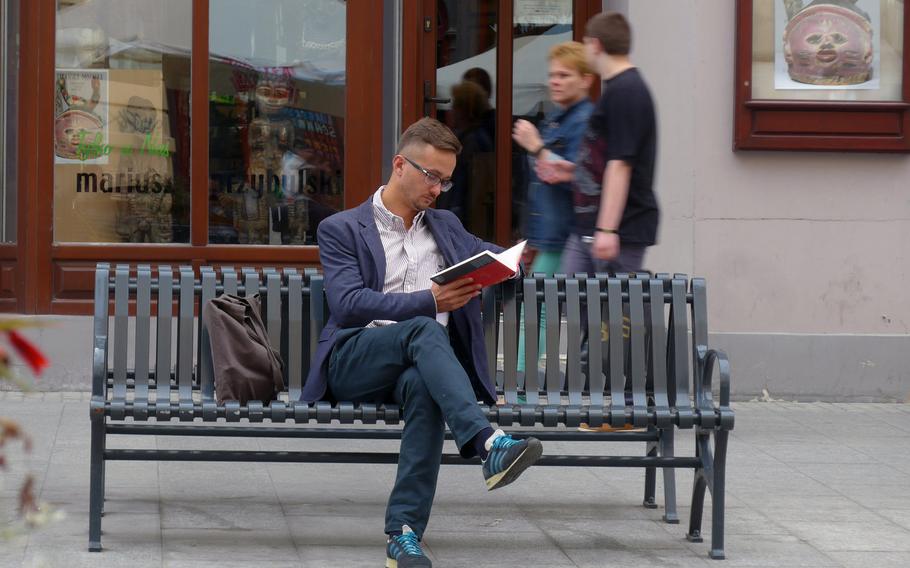 A man sits on a bench reading a book, on Piotrkowska Street in downtown Lodz, Poland.