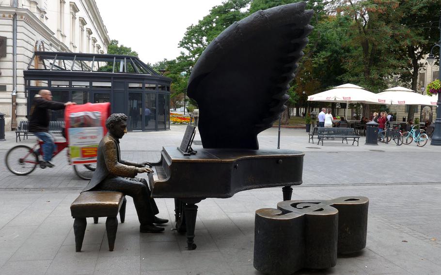 A statue of Arthur Rubinstein, the famous Polish-American pianist, stands on Piotrkowska Street in Lodz, Poland, the city of his birth. Behind it, a bicycle rickshaw rushes past.