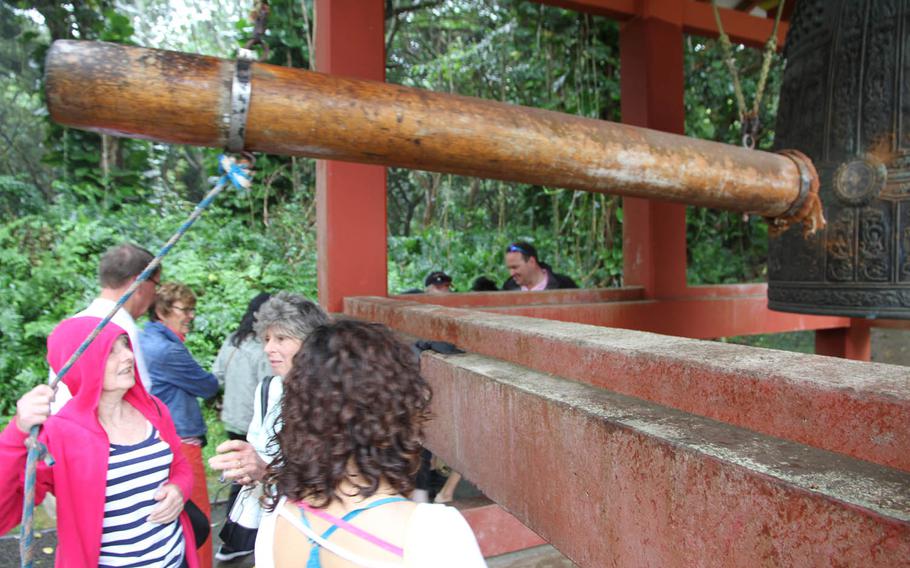 A woman pulls on a rope to gong the massive brass bell at Byodo-in Temple in Oahu, Hawaii.