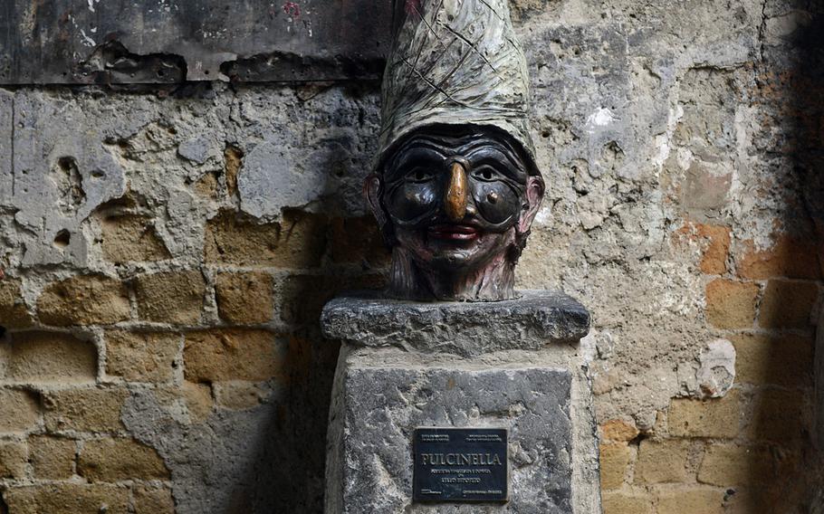 A bust of the city mascot, tragicomic clown Pulcinella, stands to the side of Via dei Tribunali.