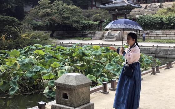A South Korean guide wearing traditional clothing explains the history of the Buyongji Pond with the Juhamnu Pavilion in the background during a tour of the Secret Garden behind the Changdeokgung Palace in Seoul, South Korea, Sunday, Oct. 8, 2017.