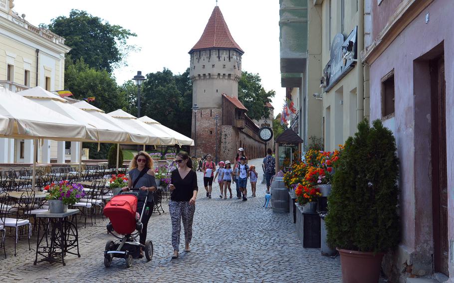 People stroll along the cobblestone lanes of Sibiu, Romania. In the background are the remnants of the city's old city fortifications with the Carpenters' Tower and the Potters' Tower.