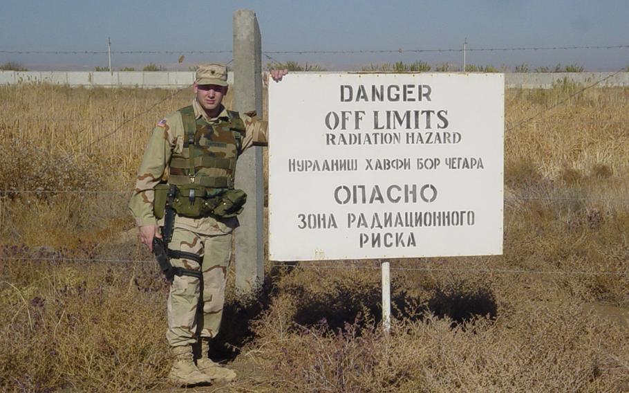 A U.S. service member stands by a sign warning of radioactivity at Karshi-Khanabad Air Base, Uzbekistan, where the U.S. had troops from 2001-2005. Many of the soldiers, airmen and Marines who deployed to the base, known as K2, have had cancer in the years since then.