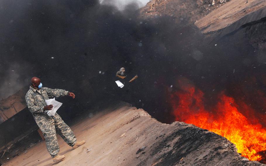 U.S. Air Force Master Sgt. Darryl Sterling tosses unserviceable uniform items into a burn pit at Balad Air Base, Iraq, on March 10, 2008. 