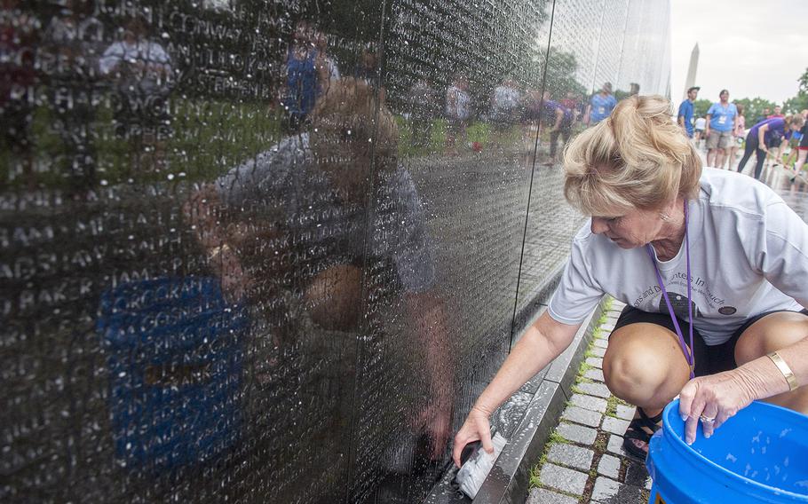 Patty Lee, daughter of Army veteran Delbert Chan Totty, scrubs the base of a granite panel on June 20, 2015, at the Vietnam Veterans Memorial Wall, where she joined dozens of volunteers for an early morning wall washing.