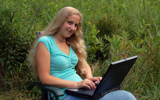 A young caucasian woman outdoors in a meadow, working on her computer